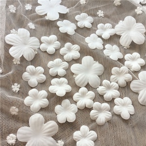 Pode incluir: Tecido branco com textura de malha e enfeites de flores brancas em 3D.