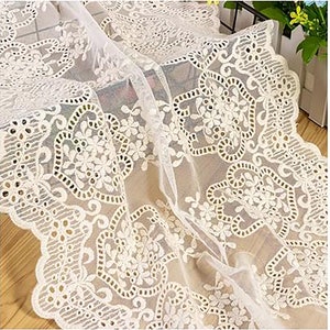 May include: White lace fabric with a delicate floral pattern. The lace has a scalloped edge and is perfect for adding a touch of elegance to any project.
