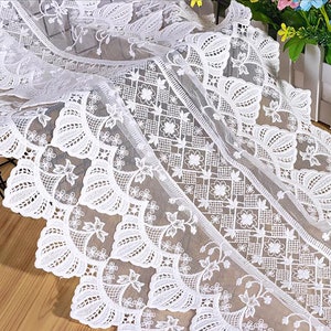 Pode incluir: Tecido de renda branca com um delicado padrão floral. A renda tem uma borda festonada e é perfeita para adicionar um toque de elegância a qualquer projeto.