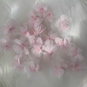 May include: Pink fabric flowers with pearl accents on a white tulle background.