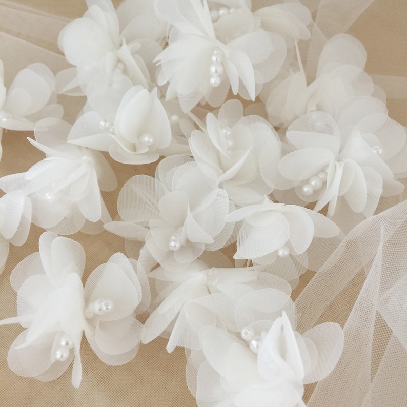 May include: A collection of white fabric flowers with pearl accents. The flowers are layered and have a delicate, airy appearance.