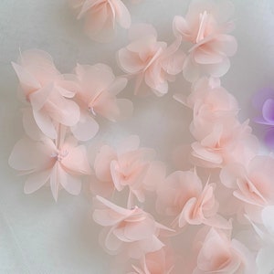 May include: A collection of delicate, pale pink fabric flowers. The flowers are layered and have a soft, airy texture.