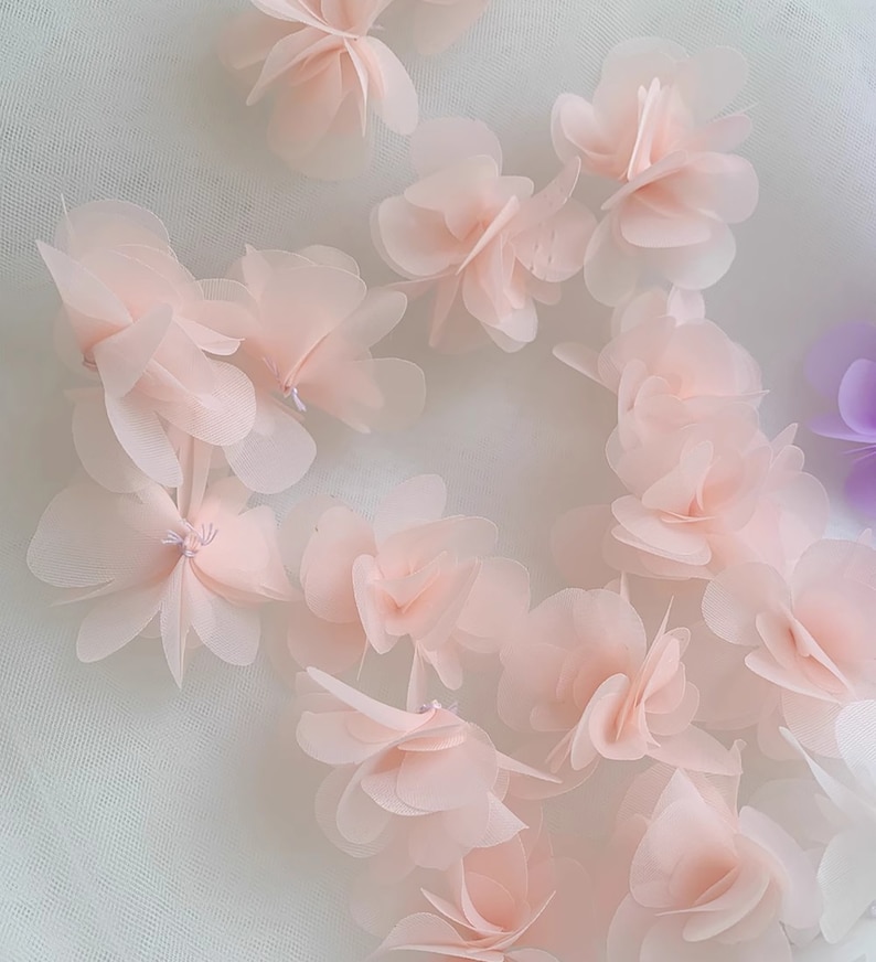 May include: A collection of delicate, pale pink fabric flowers. The flowers are layered and have a soft, airy texture.