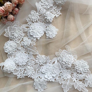Puede incluir: Borde de encaje blanco con adornos florales 3D. El encaje presenta delicados patrones florales y detalles de flores en relieve.