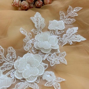 Puede incluir: Aplique de encaje floral blanco con cuentas con un diseño delicado. El encaje presenta flores y hojas tridimensionales.