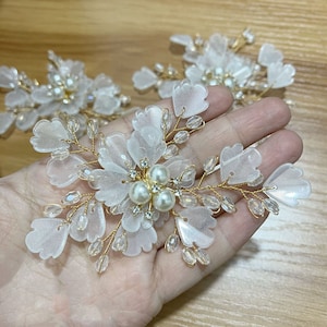Puede incluir: Peine de pelo floral blanco con detalles de perlas y alambre dorado. El peine está hecho de plástico translúcido y tiene un diseño delicado y femenino.