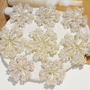 May include: Nine gold and clear crystal flower-shaped embellishments. Each embellishment has a centre with a starburst design and is surrounded by a ring of smaller crystals.