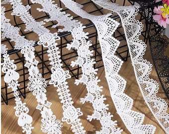 May include: A collection of white lace trims with different patterns and designs. The trims are arranged in a grid pattern on a black wire rack.