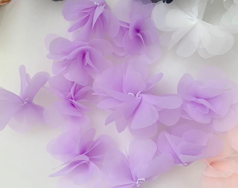 May include: A collection of lavender-coloured fabric flowers. The flowers are made of a sheer, delicate material and have a layered, ruffled appearance.