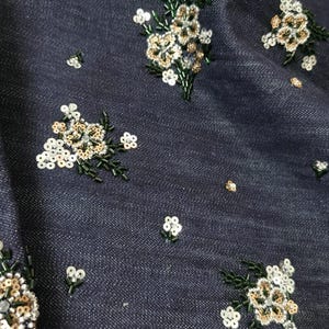 May include: Dark blue denim fabric with white and gold floral embroidery. The flowers are made of sequins and beads.