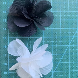 May include: Two fabric flowers, one black and one white, on a green cutting mat. The flowers are made of multiple layers of fabric and have a ruffled appearance.