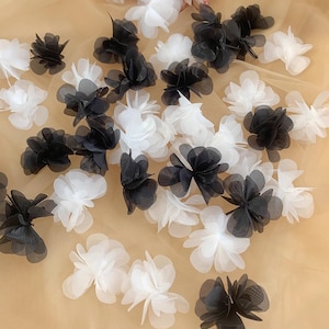 May include: A collection of black and white fabric flower embellishments. The flowers are made of layered tulle and have a delicate, ruffled appearance.