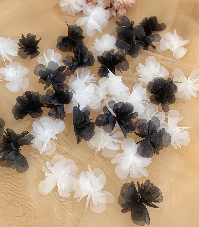 May include: A collection of black and white fabric flower embellishments. The flowers are made of layered tulle and have a delicate, ruffled appearance.
