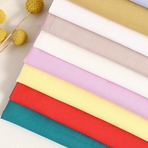 May include: A stack of eight fabric swatches in various colors, including teal, red, yellow, light pink, white, beige, and brown. The fabric is smooth and appears to be a lightweight cotton.