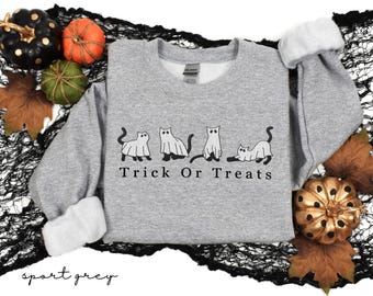May include: Sport grey sweatshirt with the text "Trick Or Treats" and a graphic of four cats in Halloween costumes. The sweatshirt is surrounded by Halloween decorations, including pumpkins and leaves.