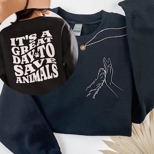 May include: Black sweatshirt with a white paw print and the text "It's a great day to save animals" on the back. The front of the sweatshirt has a white outline of a hand giving a high five to a paw.