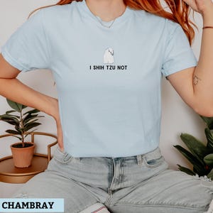 May include: Light blue t-shirt with the phrase "I Shih Tzu Not" and a small illustration of a Shih Tzu dog. The shirt is made of a soft material and has a crew neck.