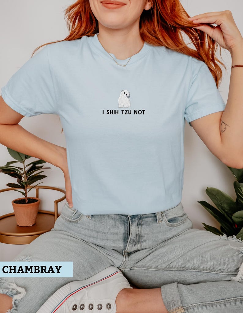 May include: Light blue t-shirt with the phrase "I Shih Tzu Not" and a small illustration of a Shih Tzu dog. The shirt is made of a soft material and has a crew neck.