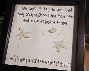 Könnte beinhalten: Gerahmtes Kunstwerk mit dem Text „How cool is it that the same God that created Oceans and Mountains and Galaxies looked at you and thought the world needed one of you too.“ Enthält zwei Seesterne und einen Stein.