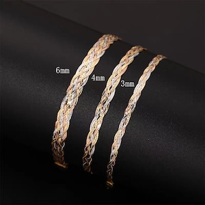 Könnte beinhalten: Drei goldene Ketten in verschiedenen Breiten, 3 mm, 4 mm und 6 mm, werden auf einer schwarzen Oberfläche gezeigt. Die Ketten sind aus geflochtenem Gold.