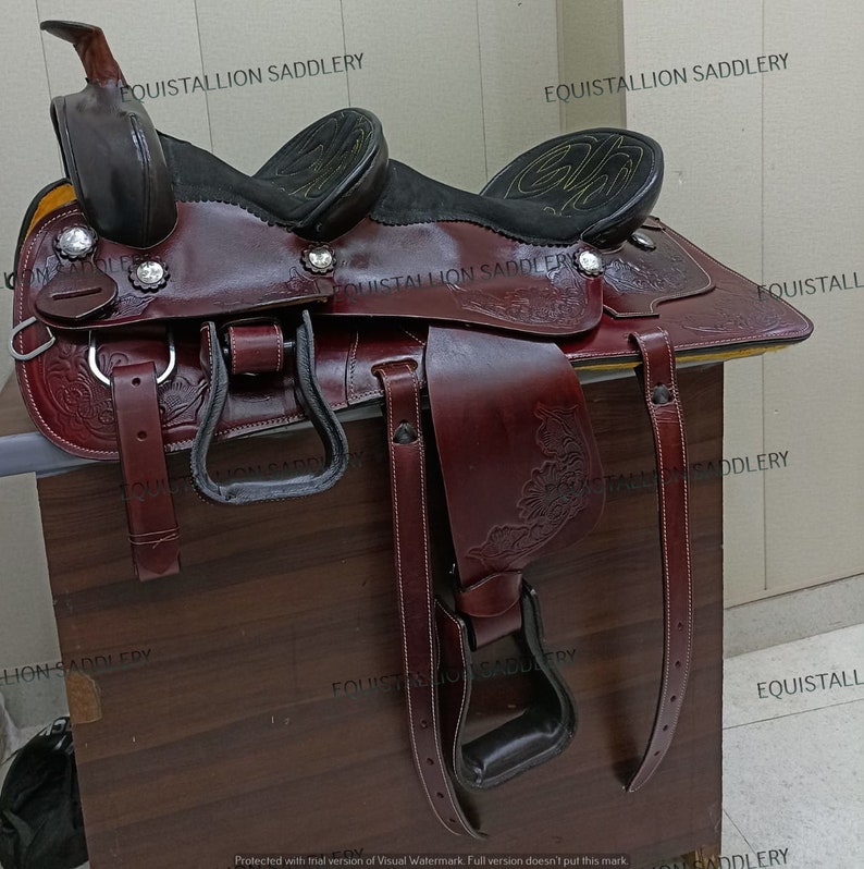 Puede incluir: Una silla de montar de cuero marr&oacute;n con intrincados detalles florales. La silla tiene un asiento negro y dos tapas de cuerno negras. La silla est&aacute; sobre una superficie de madera. El texto "EQUISTALLION SADDLERY" es visible en la silla.