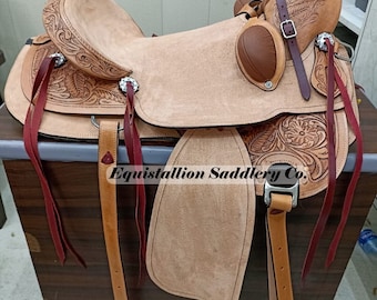 May include: A tan leather saddle with intricate tooling and a burgundy leather skirt. The saddle is on a wooden stand and has a silver concho on the cantle. The saddle is labeled "Equistallion Saddlery Co."