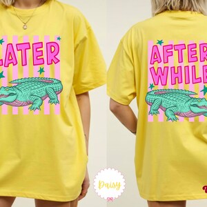 K&ouml;nnte beinhalten: Gelbes T-Shirt mit einem vorderen Aufdruck &bdquo;LATER&ldquo; und einem hinteren Aufdruck &bdquo;AFTER WHILE&ldquo;. Beide Grafiken zeigen ein gr&uuml;nes Alligatordesign mit rosa und gr&uuml;nen Akzenten.