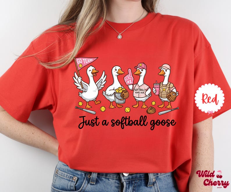 May include: Red t-shirt with a graphic of four cartoon geese playing softball. The geese are wearing baseball caps, holding a pennant, a foam finger, a drink, and a catcher's mitt. The text "Just a softball goose" is below the geese.