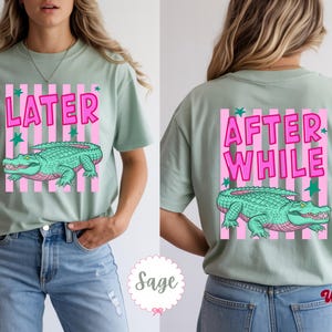 K&ouml;nnte beinhalten: Salbeigr&uuml;nes T-Shirt mit einem gr&uuml;nen Alligator-Design, rosa Streifen und dem Wort "LATER" in Pink. Auf der R&uuml;ckseite steht "AFTER WHILE" und ein passendes Alligator-Design. Ein l&auml;ssiger, bequemer Stil.