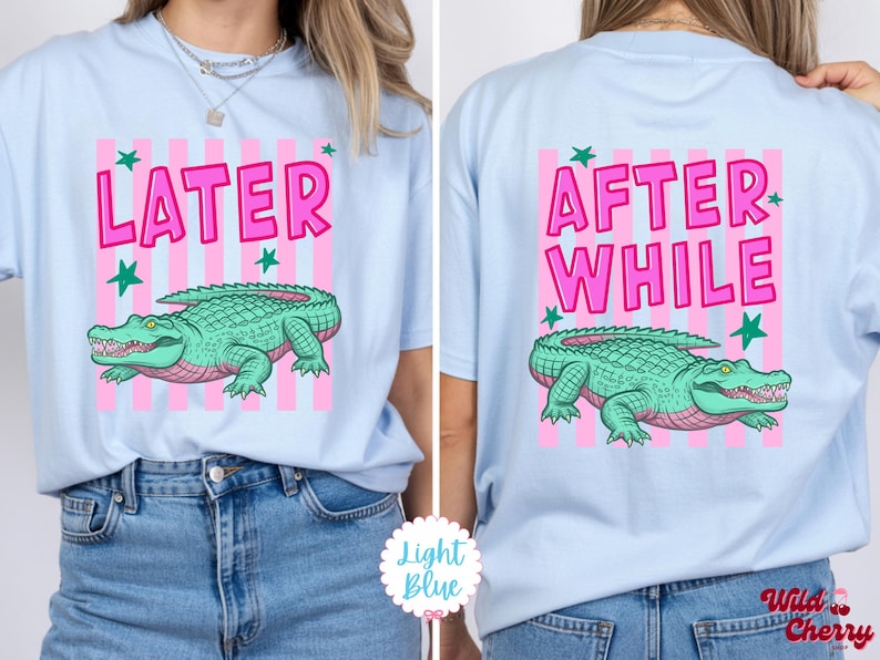 K&ouml;nnte beinhalten: Hellblaues T-Shirt mit rosa und wei&szlig;en Streifen. Auf der Vorderseite steht das Wort "LATER" in Pink, ein gr&uuml;nes Alligator und gr&uuml;ne Sterne. Auf der R&uuml;ckseite stehen die Worte "AFTER WHILE" und ein gr&uuml;nes Alligator.