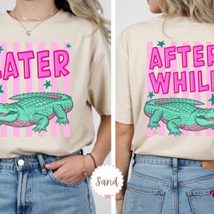 K&ouml;nnte beinhalten: Beiges T-Shirt mit rosa und wei&szlig;en Streifen. Auf der Vorderseite des Shirts steht das Wort "LATER" in Pink, mit einer gr&uuml;nen Alligator-Illustration. Auf der R&uuml;ckseite des Shirts stehen die Worte "AFTER WHILE" in Pink, mit einer gr&uuml;nen Alligator-Illustration.