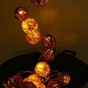 Könnte beinhalten: Eine Lichterkette mit warmweißen LED-Lichtern und runden, geflochtenen Papierkugeln. Die Lichter hängen über einem schwarzen Wok.