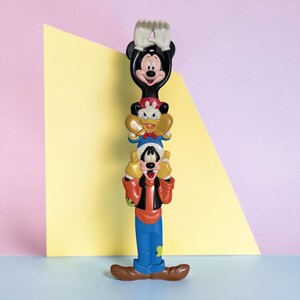 May include: A vertical plastic figurine stack featuring Mickey Mouse at the top with arms raised, Donald Duck in the middle, and Goofy at the base. The characters are rendered in their classic colours of black, white, red, yellow, blue, and brown.