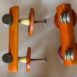 May include: Two wooden cabinet knobs with a brown finish and silver accents. The knobs have a rounded rectangular shape and are attached to a metal screw.