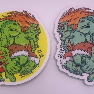 May include: Two green and orange stickers of a cartoon monster with the text "21 19" on the sticker. The monster is green with orange hair and is holding a brown object.