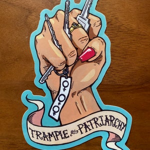 May include: A blue and pink sticker with a raised fist holding keys and a keychain with the female symbol. The banner reads "TRAMPLE the PATRIARCHY".