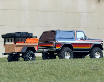 May include: A black and orange toy truck with a black and brown trailer. The truck has a black roof and a red, orange, and yellow stripe on the side. The trailer has a black metal cage and a brown wooden bed.