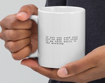 Może przedstawiać: Biały ceramiczny kubek z czarnym tekstem w stylu maszyny do pisania o treści: If you can read this you're way too close to me this early in the morning. Kubek ma standardowy cylindryczny kształt z zakrzywionym uchwytem z boku.