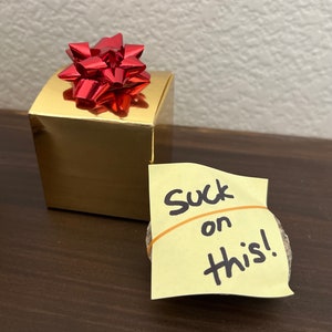 „Suck on this” z płyty Goodbye Toby’ego w opakowaniu prezentowym — żart biurowy