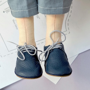 Puede incluir: Un par de zapatos de cuero azul oscuro con cordones grises. Los zapatos están atados y tienen una punta redonda.