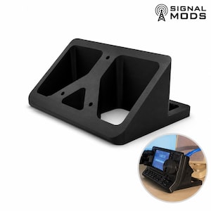 May include: A black angled stand with two compartments and a triangular cutout. The stand has a rectangular base and is designed to hold electronic devices. The Signal Mods logo is in the upper right corner.