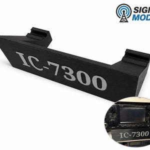 以下が含まれることがあります： シルバーの文字で「IC-7300」と書かれた黒い角度付きブラケット。ブラケットはテクスチャ加工された表面を持ち、ラジオを保持するように設計されています。円形のインセットは、使用中のラジオとブラケットを示しています。Signal Modsのロゴは右上隅にあります。