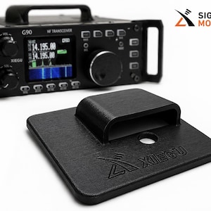 May include: A black HF transceiver with a digital display showing frequency readings, paired with a black base with the XIEGU logo. The transceiver has multiple knobs and buttons. The Signal Mods logo is in the upper right corner.