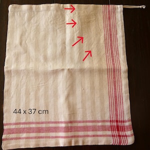 Op de afbeelding: Cr&egrave;mekleurige linnen tas met rode strepen en een trekkoordsluiting. De tas meet 44 x 37 cm en heeft verticale strepen op het hoofdgedeelte en horizontale strepen aan de onderkant. De tas is waarschijnlijk bedoeld voor opslag of het dragen van items.