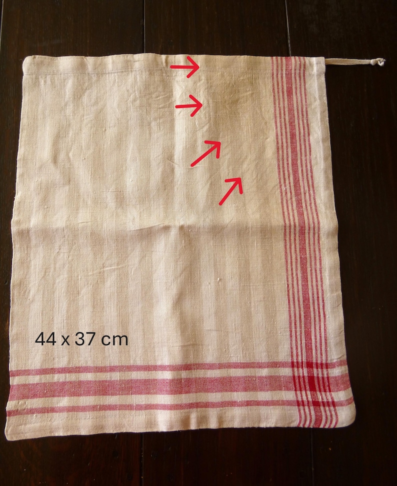 Op de afbeelding: Cr&egrave;mekleurige linnen tas met rode strepen en een trekkoordsluiting. De tas meet 44 x 37 cm en heeft verticale strepen op het hoofdgedeelte en horizontale strepen aan de onderkant. De tas is waarschijnlijk bedoeld voor opslag of het dragen van items.