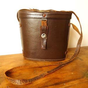 May include: A brown leather binocular case with a strap. The case has a metal clasp and a flap with a metal button.