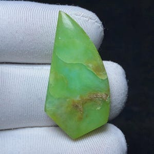 May include: A polished, teardrop-shaped gemstone featuring a vibrant lime green colour with translucent areas and natural, earthy brown inclusions. The stone has a smooth, glossy surface and a pointed top, showcasing a unique, organic pattern.
