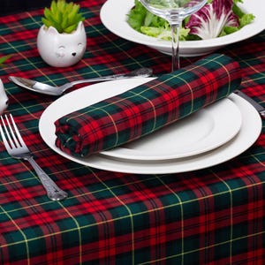 Puede incluir: Un mantel de cuadros rojos y verdes con un plato blanco, una servilleta y un tenedor. Hay dos pequeñas macetas de cerámica blanca con plantas verdes en la mesa.