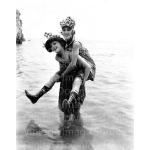 Könnte beinhalten: Vintage Schwarz-Weiß-Fotografie von zwei Frauen im Meer. Eine Frau trägt die andere auf dem Rücken. Beide Frauen tragen Hüte und Stiefel. Sie lächeln und scheinen Spaß zu haben.
