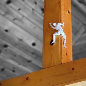 May include: A white, three-dimensional figure of a person climbing, mounted on a vertical wooden beam. The figure is depicted in a dynamic pose with limbs extended as if scaling the wood. The text kamy3d.etsy.com is visible on the beam.